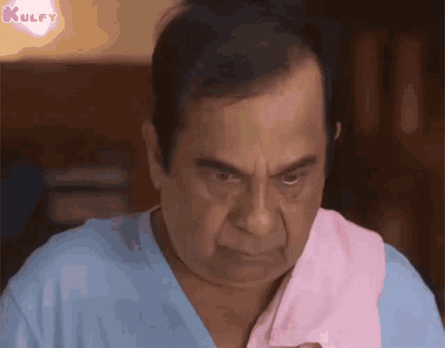 a man wearing a blue shirt and a pink towel around his neck is making a face .
