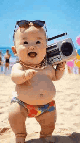 the baby is wearing sunglasses and holding a boombox on the beach .