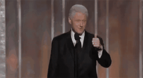 a man in a suit and tie is giving a thumbs up sign .