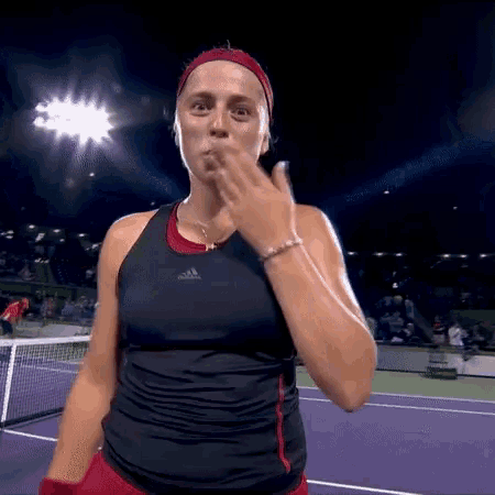 a woman is blowing a kiss while standing on a tennis court