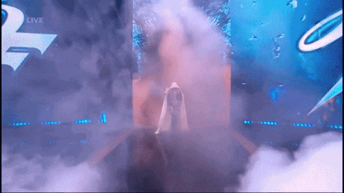 a woman in a white dress is standing in front of a stage with smoke coming out of it and a sign that says live