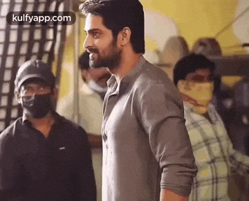 a man with a beard wearing a mask is standing in a room with other men .