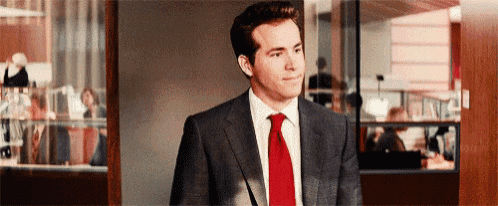 a man in a suit and red tie is standing in front of a window .