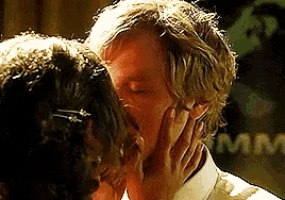a man and a woman are kissing and the man is covering his face with his hand .