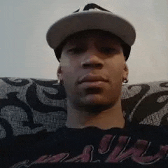 a man wearing a hat and earrings is sitting on a couch and looking at the camera .