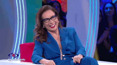 a woman wearing glasses and a blue suit is sitting on a red couch and smiling