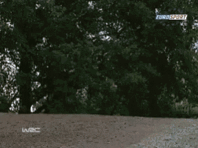 a yellow car is driving down a dirt road with trees in the background and the word wbc on the bottom