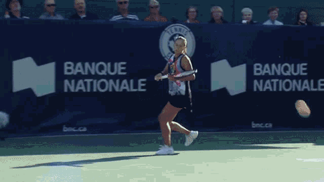 a woman bending over holding a tennis racquet in front of a banner that says canada
