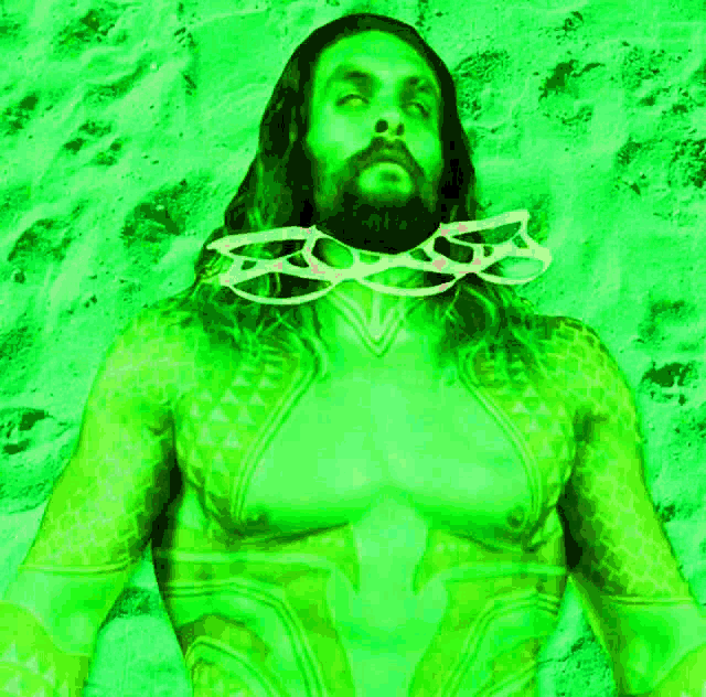 a man with long hair and a beard is standing on a beach wearing glasses .