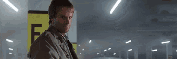 a man in a trench coat is standing in a dark room in front of a yellow sign that says f.