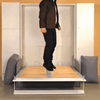a man in a brown jacket is jumping on top of a bed .