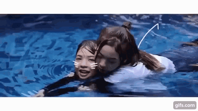 two girls are swimming in a pool together and one of them is hugging the other .