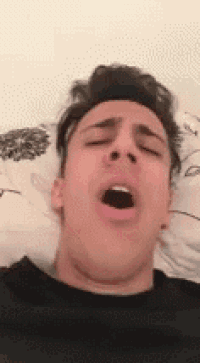 a man is yawning in bed with his mouth open .