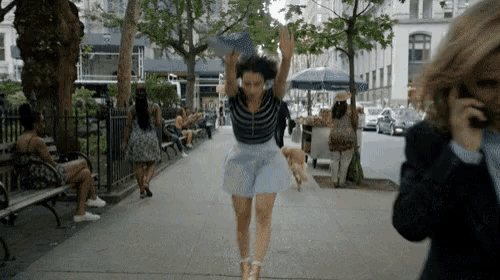 a woman in a blue skirt is jumping in the air while a man talks on a cell phone