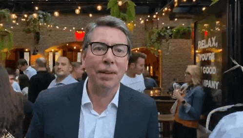 a man in a suit and glasses is standing in front of a sign that says relax you 're a good company