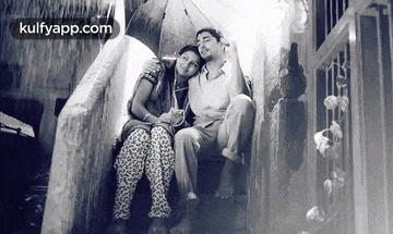 a black and white photo of a man and woman sitting under an umbrella with the website kulfyapp.com in the corner
