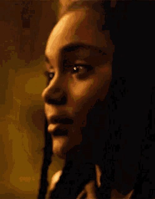 a close up of a woman 's face with braids in her hair and a dark background .