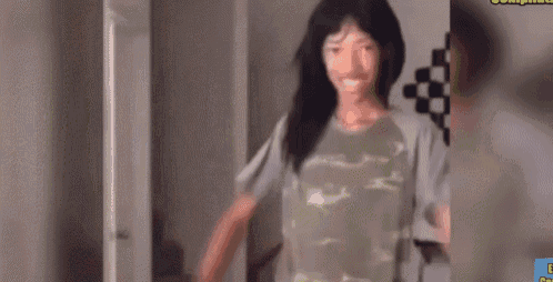 a woman wearing a camouflage shirt is standing in a room and smiling .