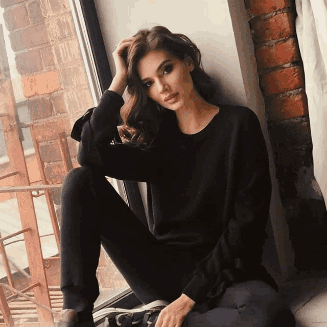 a woman in a black sweater sits on a window sill