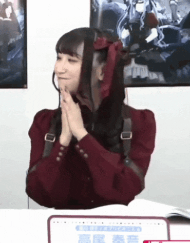 a woman wearing a red jacket is sitting at a table with her hands folded