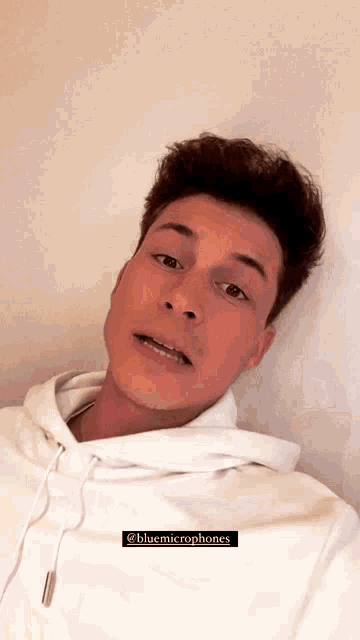 a young man wearing a white hoodie is taking a selfie with a caption that says bluemicrophones