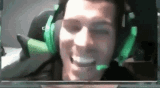 a man wearing headphones and glasses is smiling while sitting in front of a computer screen .