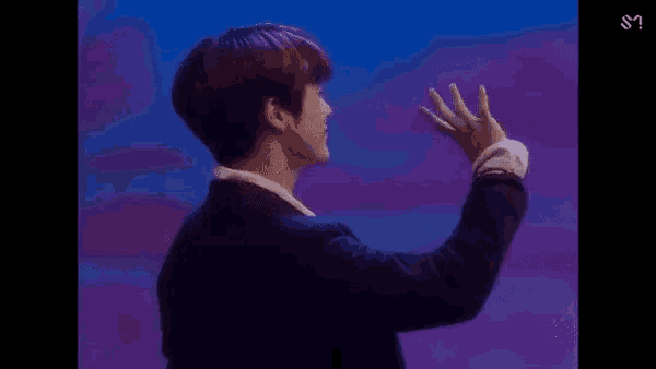 a man in a suit is waving his hand in front of a blue background .