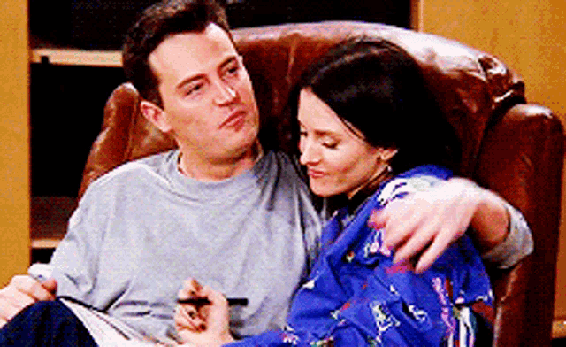 a man and a woman are sitting in a chair and the woman is holding the man 's arm