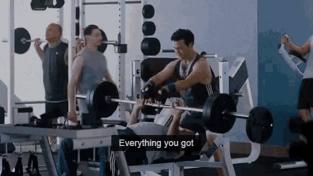 a man is lifting a barbell in a gym while another man watches .