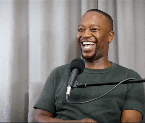 a man laughs in front of a microphone while wearing a green shirt
