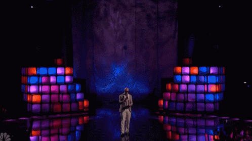 a man in a suit sings into a microphone on a stage with purple lights