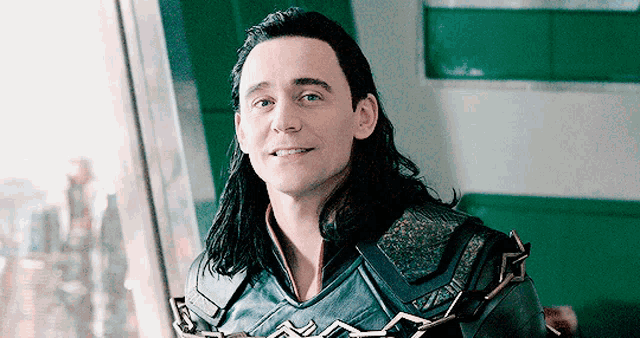 a man with long hair and a chain around his neck is smiling and looking out a window .
