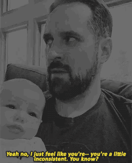 a man with a beard is holding a baby and says yeah no