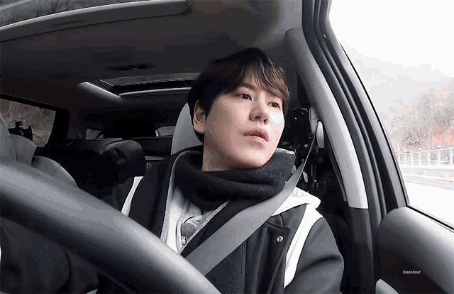 a man wearing a scarf is sitting in a car with a seat belt around his neck