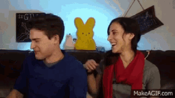 a man and a woman are sitting on a couch and the woman is laughing