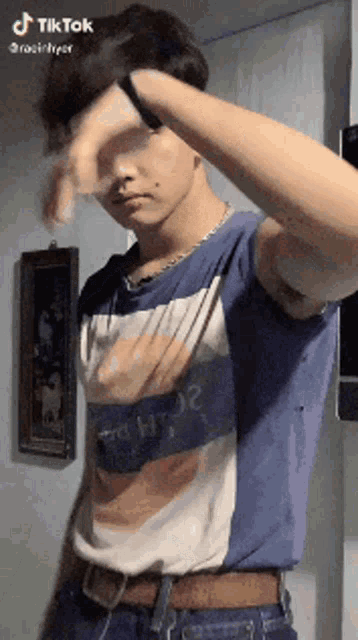 a young man wearing a blue and white shirt is standing in front of a wall with his hand on his face .