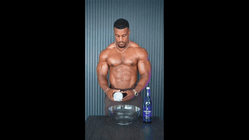 a shirtless man is sitting in front of a bowl of ice next to a bottle of vodka .