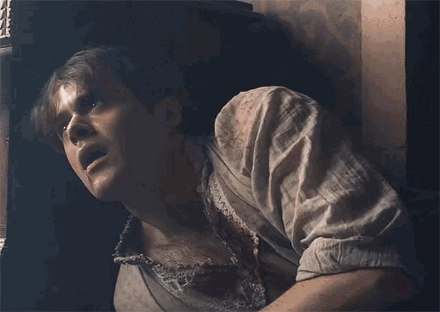 a man in a dirty shirt is standing in a dark room with his mouth open