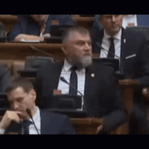 a man with a beard is sitting at a podium in a parliament