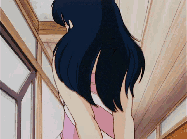 a girl with long black hair is standing in a hallway with her back to the camera