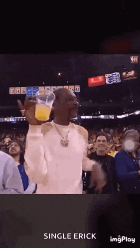 snoop dogg is holding a cup of orange juice in his hand while watching a basketball game .
