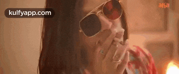 the woman is wearing sunglasses and covering her mouth with her hand .