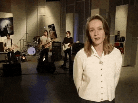 a woman in a white shirt is standing in front of a band in a studio .