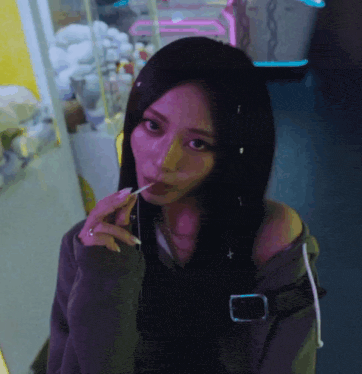 a woman with long black hair is eating a lollipop and looking at the camera