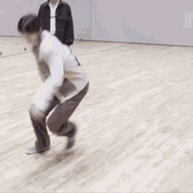 a man is dancing on a wooden floor while another man watches .