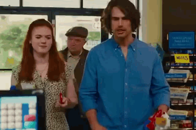 a man and a woman are standing in a store . the man is wearing a blue shirt .