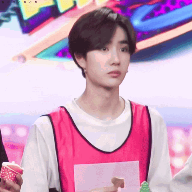 a young man wearing a pink vest and a white shirt looks at the camera