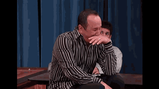 a man in a black and white striped shirt is sitting down