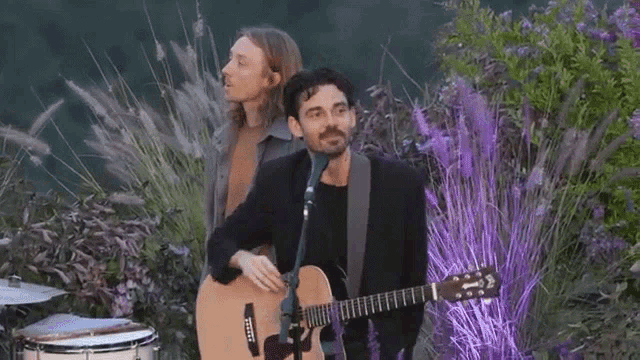 a man playing an acoustic guitar next to another man playing drums