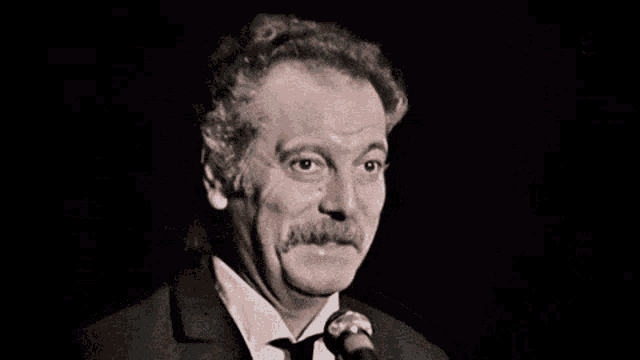 a man in a suit and tie is speaking into a microphone .